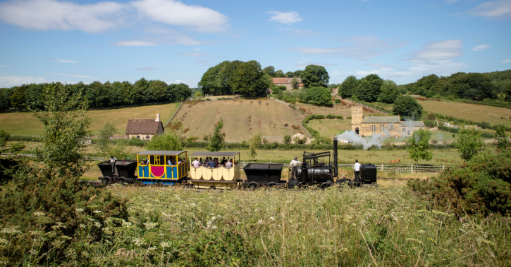 Replica steam engine with carriages pulling people through the 1820s landscape at Beamish Museum